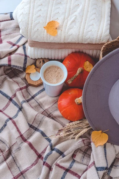 Cozy autumn still life. Cup of coffee, knitted plaid, pumpkins and autumn leaves on white wooden background.