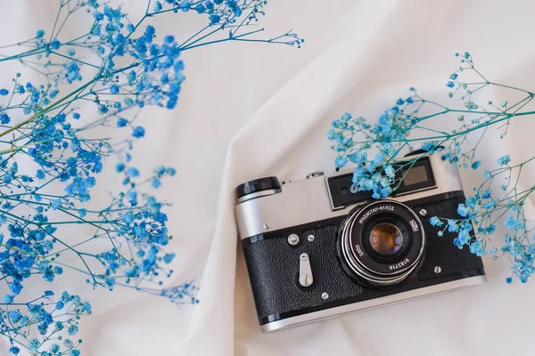 Beyaz kumaş üzerinde klasik kamera ve mavi çigila çiçekleri