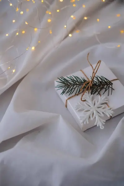 Noel hediyesi kutusunda köknar ağacı dalı ve beyaz kumaş arka planında kar tanesi var.