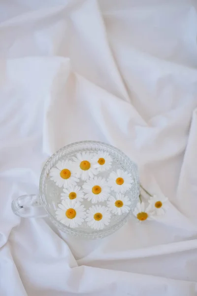 stock image Chamomile flowers in a glass bowl on white fabric background