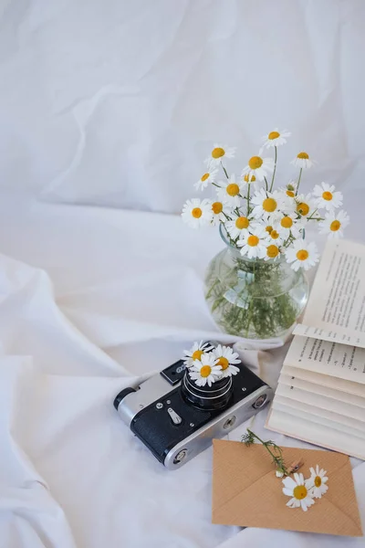 Vazoda papatya çiçekleri, klasik kamera ve beyaz kumaş üzerine kitap..