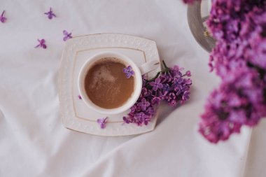 Beyaz arka planda leylak çiçekli bir fincan kahve..