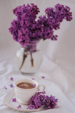 Beyaz arka planda leylak çiçekli bir fincan kahve..
