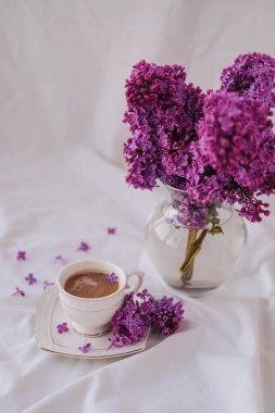 Beyaz arka planda leylak çiçekli bir fincan kahve..