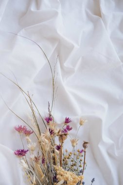 Beyaz kumaş arka planda kurumuş çiçek demeti.