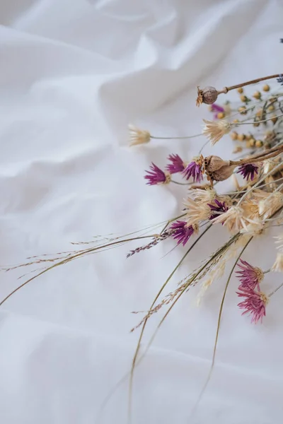 Bouquet of dried flowers on white fabric background.
