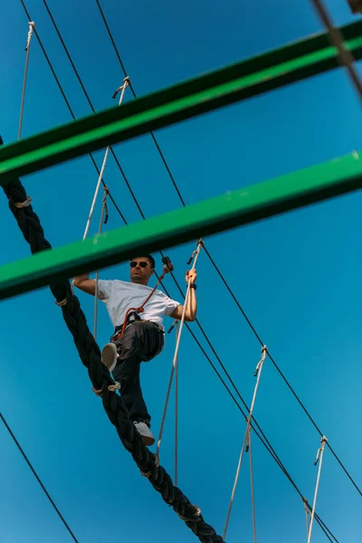 アドベンチャーパークのシングルロープブリッジを簡単に行くハンサムな訓練を受けた男 — ストック写真