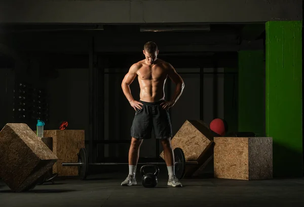 Full-length photo of a handsome man with a naked torso exercising with a kettlebell on a dark background