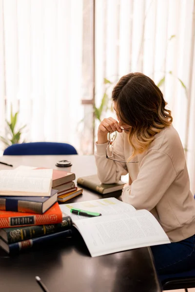 Hermosa Chica Estudiando Escritorio Una Biblioteca Mientras Sostiene Sus Gafas — Foto de Stock