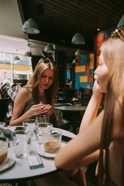 两个年轻美丽的女孩坐在商场的咖啡店里聊天 — 图库照片