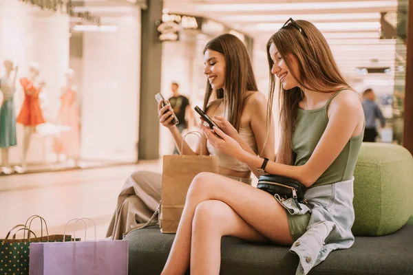 Две Красивые Девушки Смотрят Свои Телефоны Сидя Диване Торговом Центре — стоковое фото