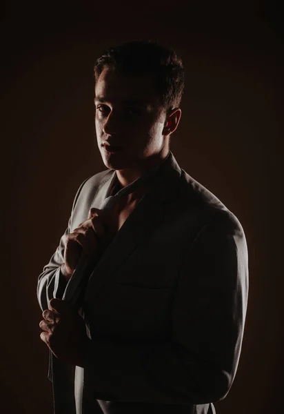 スタジオに立っている間に彼のネクタイを固定ハンサムな男のシルエット — ストック写真
