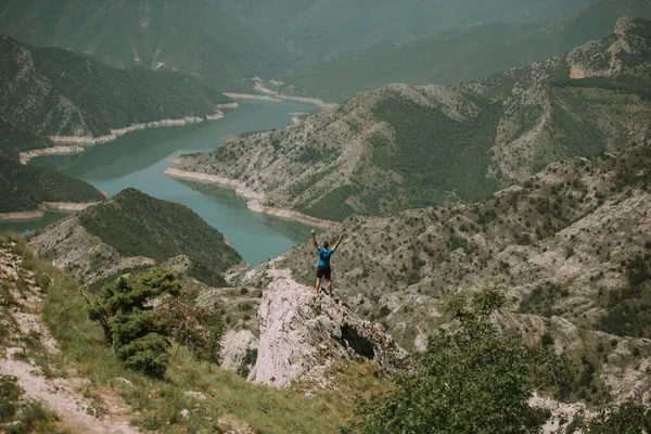 身穿蓝色衬衫的男人高举双臂站在山顶上 — 图库照片