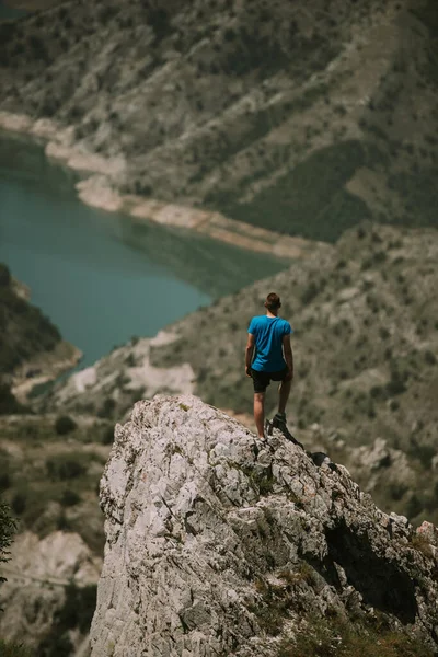 穿着蓝色衬衫站在山顶看着湖面的男人 — 图库照片