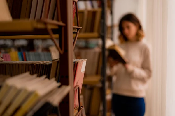 一个女大学生站在图书馆的书架上看书时 弄糊涂了 — 图库照片