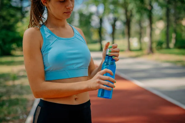 Female sportsperson opening a bottle of water while standing on a sports track in the park
