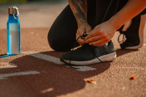 A picture of young male sportsperson tying his shoelaces. He put the bottle of water on the ground next to him