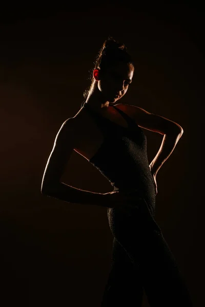 スタジオでポーズをとっている黒のキラキラしたオーバーオールを身に着けている少女のシルエット 背骨に手を — ストック写真