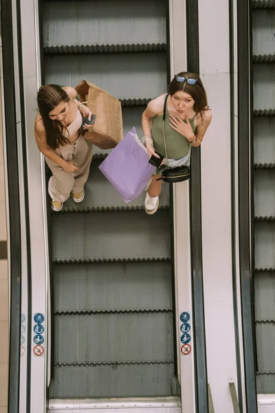 Zwei Hübsche Mädchen Mit Einkaufstüten Auf Der Rolltreppe — Stockfoto