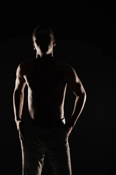 SIlhouette of black male is posing with his hands in the pocket while posing on dark background