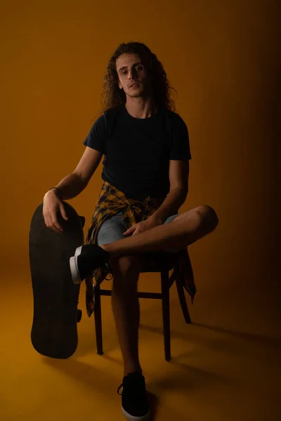 Jovem Bonito Macho Sentado Uma Cadeira Descansando Mão Skate Estúdio — Fotografia de Stock