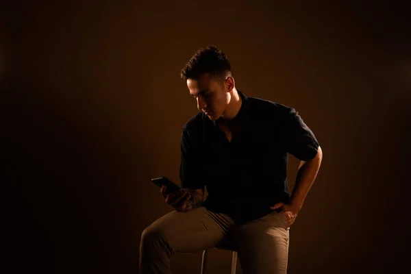 Όμορφος Άντρας Κοιτάζει Τηλέφωνό Του Ενώ Κάθεται Στο Στούντιο — Φωτογραφία Αρχείου