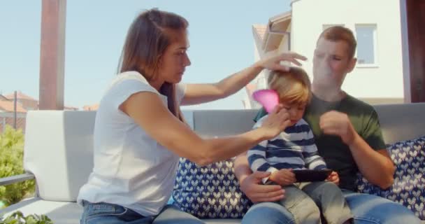 美丽的母亲在梳理她儿子的头发 而父亲则抱着他 — 图库视频影像
