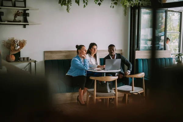 三个商人坐在咖啡店的蓝色沙发上 一边看着笔记本电脑 — 图库照片