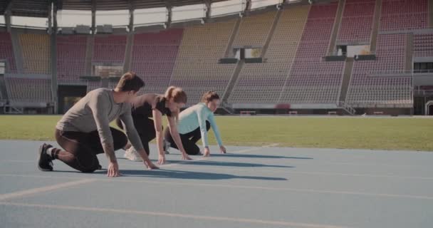 三个年轻人准备在一个空荡荡的体育场的跑道上比赛 — 图库视频影像