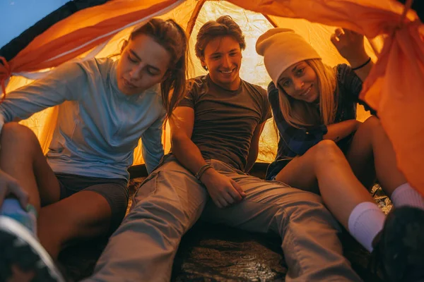 Three friends hanging out while sitting in the orange tent