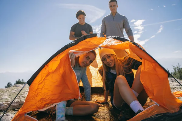 Две Симпатичные Девушки Сидят Оранжевой Палатке Пока Парни Стоят — стоковое фото