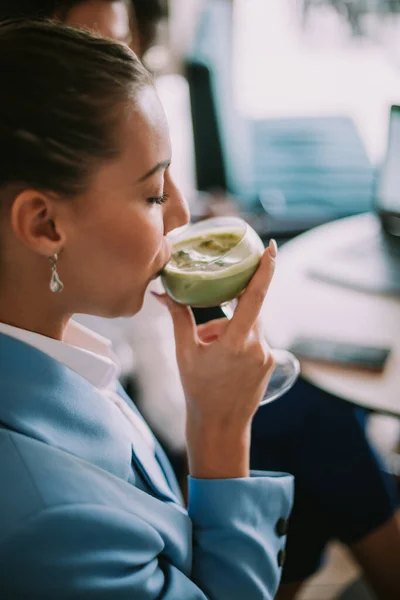 Close up of beautiful business woman drinking matcha latte while sitting at the cafe
