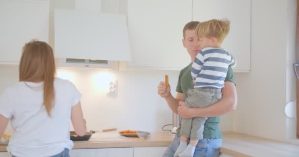 Father Son Talking Eating Fish Strips While Mother Cooking Kitchen — Video