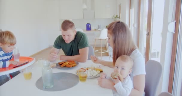 ダイニングテーブルのダイニングルームで子供たちと昼食を食べながら会話をする両親 — ストック動画