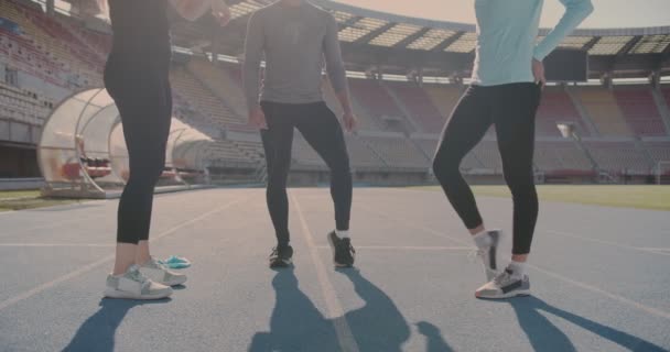 Троє Людей Розтягуються Крутяться Ногами Щоб Підготуватися Бігу Стадіоні — стокове відео