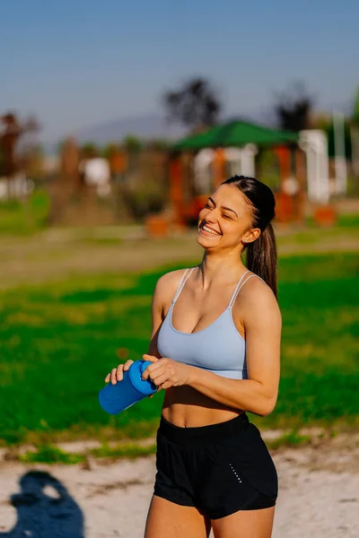 A beautiful female sports person is laughing after funny conversation with her boyfriend. She is holding a bottle of water in her hands