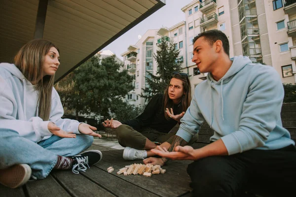 Three Friends Sitting Wooden Bench While Making Faces Scattered Jenga — Stock fotografie
