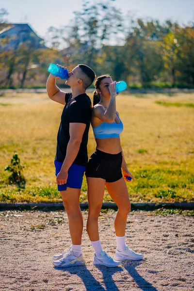 Fit couple standing back to back and drinking water