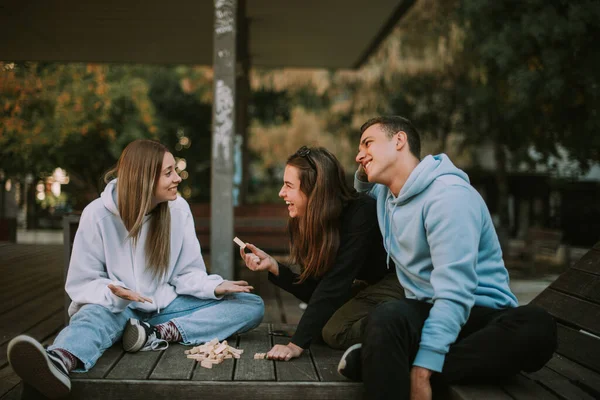 Three Happy Friends Sitting Wooden Bench Scattered Jenga — Stockfoto