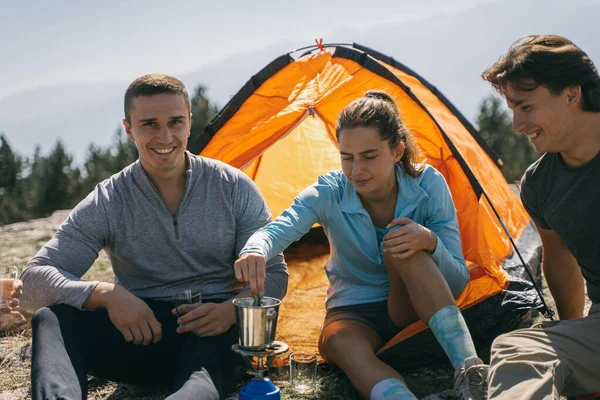 Close up of three friends smiling and making coffee while sitting infront of the tent