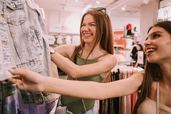 Two beautiful girls laughing while looking trough the clothes in the shop