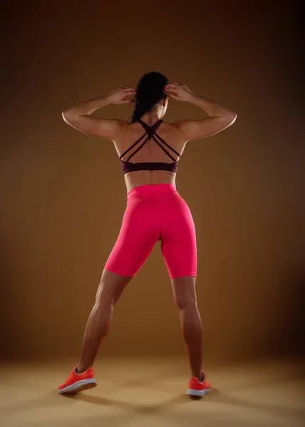 A back view photo of fit woman posing with her hands behind the head. Full length photo
