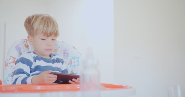 Közelkép Aranyos Kisfiú Rágás Nézi Telefonját Miközben Gyerek Szék — Stock videók