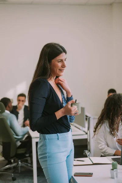 Close up of beautiful brunette business girl holding her coffee cup while standing and looking at someone at the office