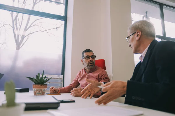 stock image Two older business men having a conversation while sitting at the desk at the co working space