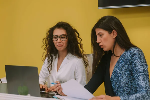 两个女商人坐在共同工作的空间里 一边看着笔记本电脑 一边聊天 — 图库照片