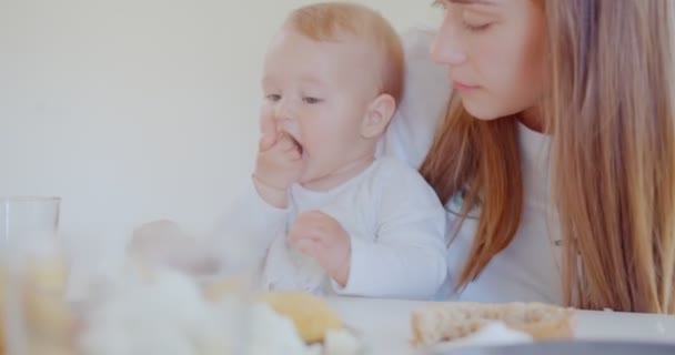 在餐桌边吃面包时 一个可爱的小女孩坐在妈妈的腿上 — 图库视频影像
