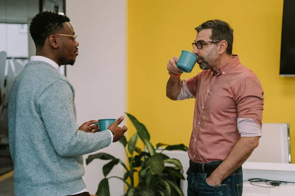 コーヒーを飲みながら休みの日に職場の同僚と話をしているハンサムな黒人が 丁寧に話を聞いている — ストック写真