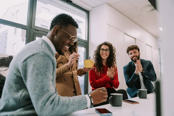 A black male person is awarded with applause by his white colleagues after giving a good idea for the new marketing strategy while having a coffee time