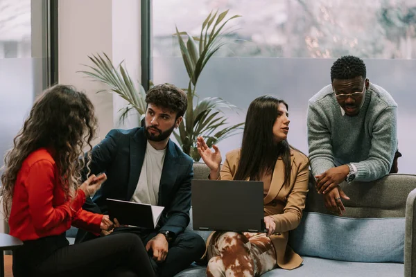 四个多种族的同事坐在一间现代办公室的灰色沙发上 在一家公司的项目上一起工作 — 图库照片